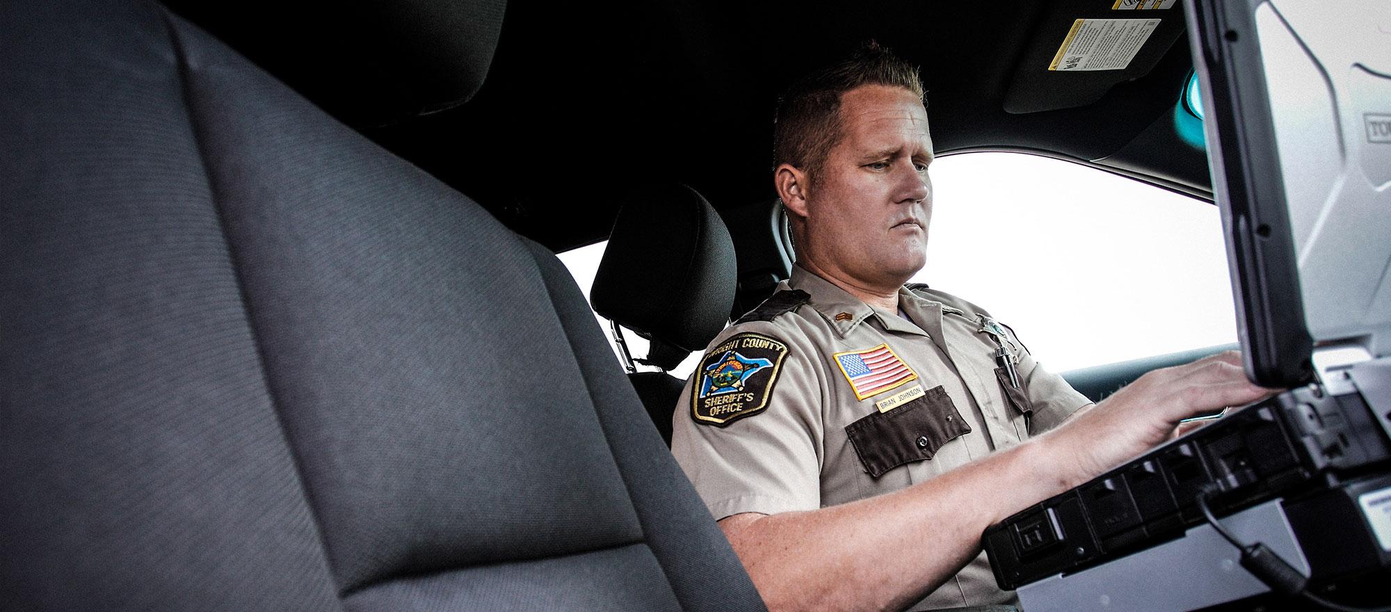 An officer in his squad car using a laptop.